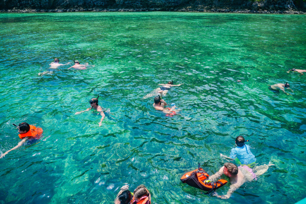 Tourists snorkeling in bright turquoise water during a daytime island hopping tour in Krabi.