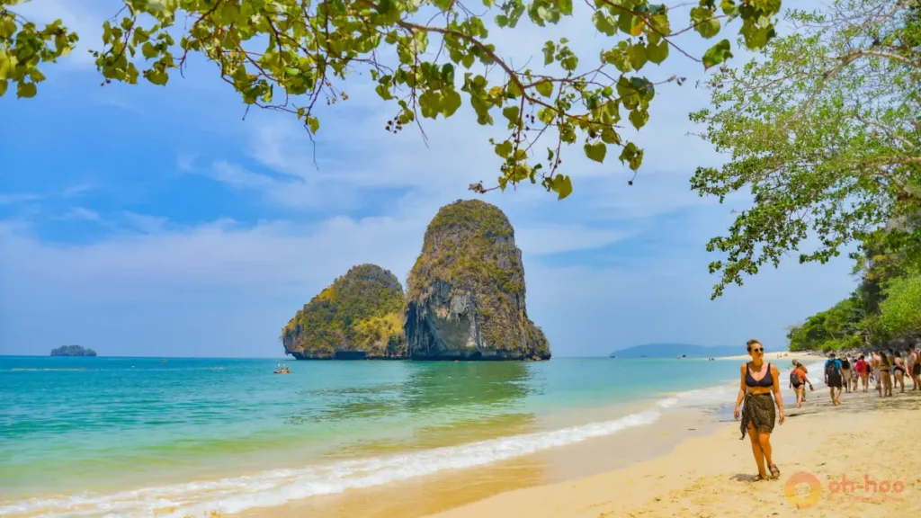 This image shows tourists walking along a tropical beach in Krabi with turquoise water, soft sand and limestone cliffs, highlighting one of the best things to do in Krabi Thailand for beach lovers, island tours and scenic coastal views.