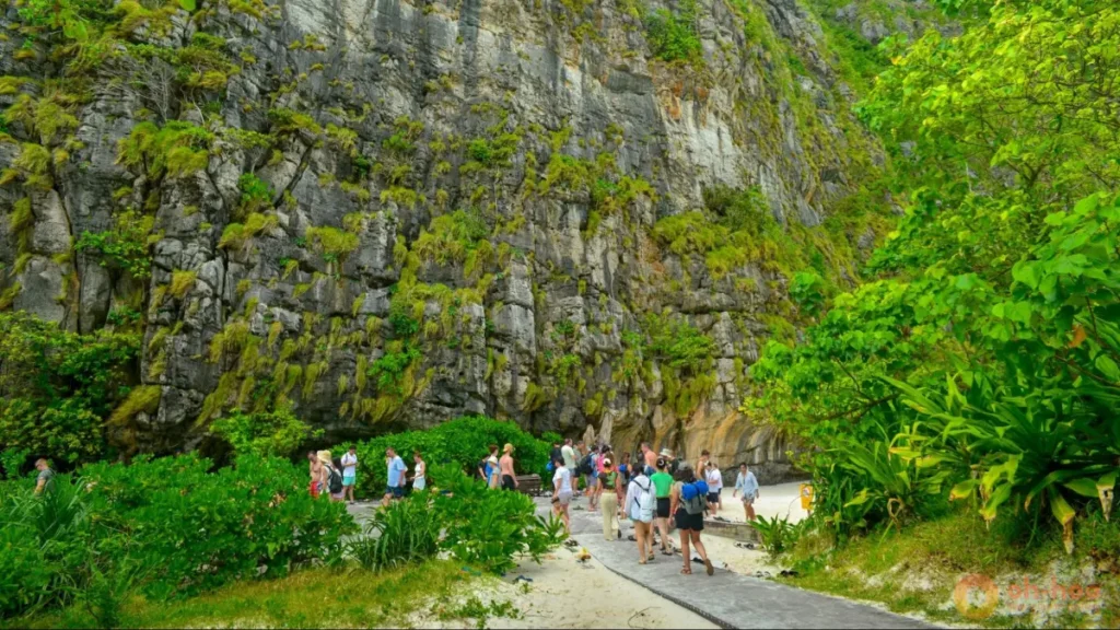 This image shows tourists exploring a limestone cliff and beach area in Krabi, Thailand, highlighting cave beaches, island tours and scenic nature walks as some of the best things to do in Krabi for families, couples and adventure travelers.