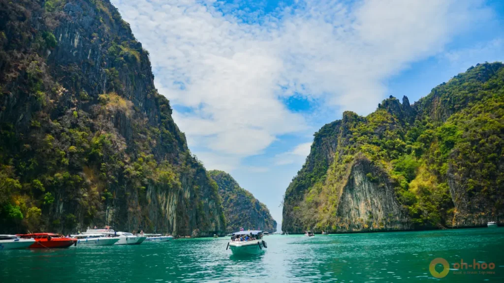 This image shows longtail boats cruising through turquoise water between dramatic limestone cliffs in Krabi, Thailand, highlighting island hopping and boat tours as one of the best things to do in Krabi for couples, families and adventure travelers.