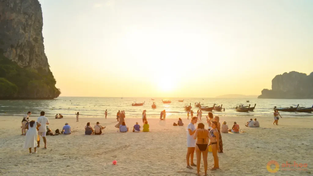This image shows travelers watching the sunset on a Krabi beach with longtail boats, limestone cliffs and golden sea views, highlighting sunset beach walks and island tours as some of the best things to do in Krabi for couples and families.