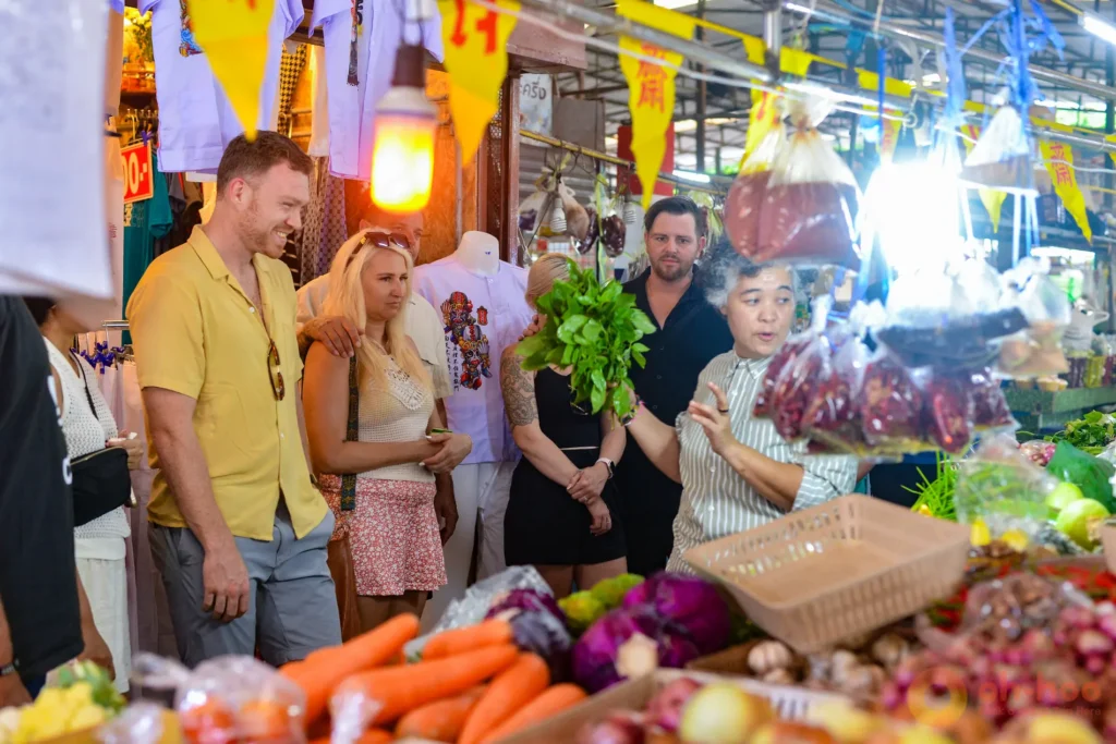 Thai chef guiding travellers through a wet market on a cooking class in Phuket