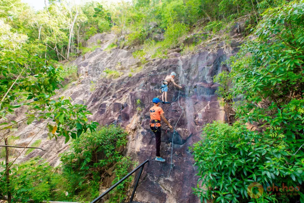 A climber on the Via Ferrata cliff route with a guide, using metal rungs and a belay line at the Koh Phangan sky park