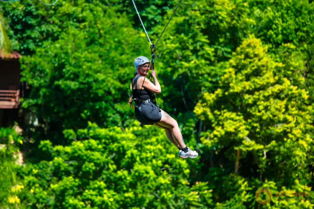 A rider in a helmet and harness soaring along the Koh Phangan zipline high over the green jungle valley