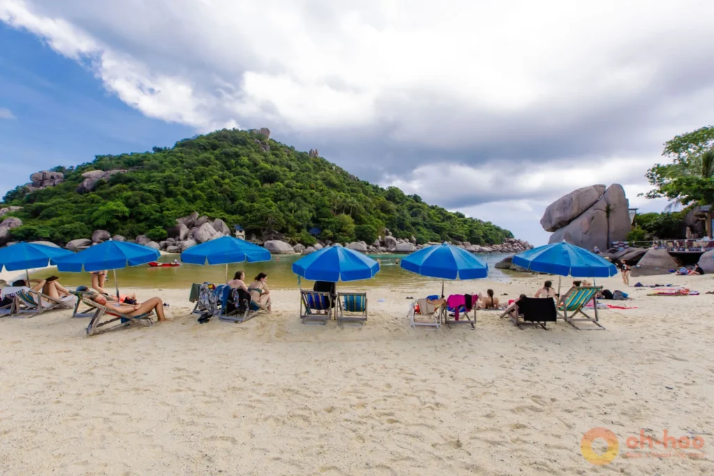 Blue beach umbrellas and deck chairs on Koh Nang Yuan's white-sand beach beside a clear turquoise bay