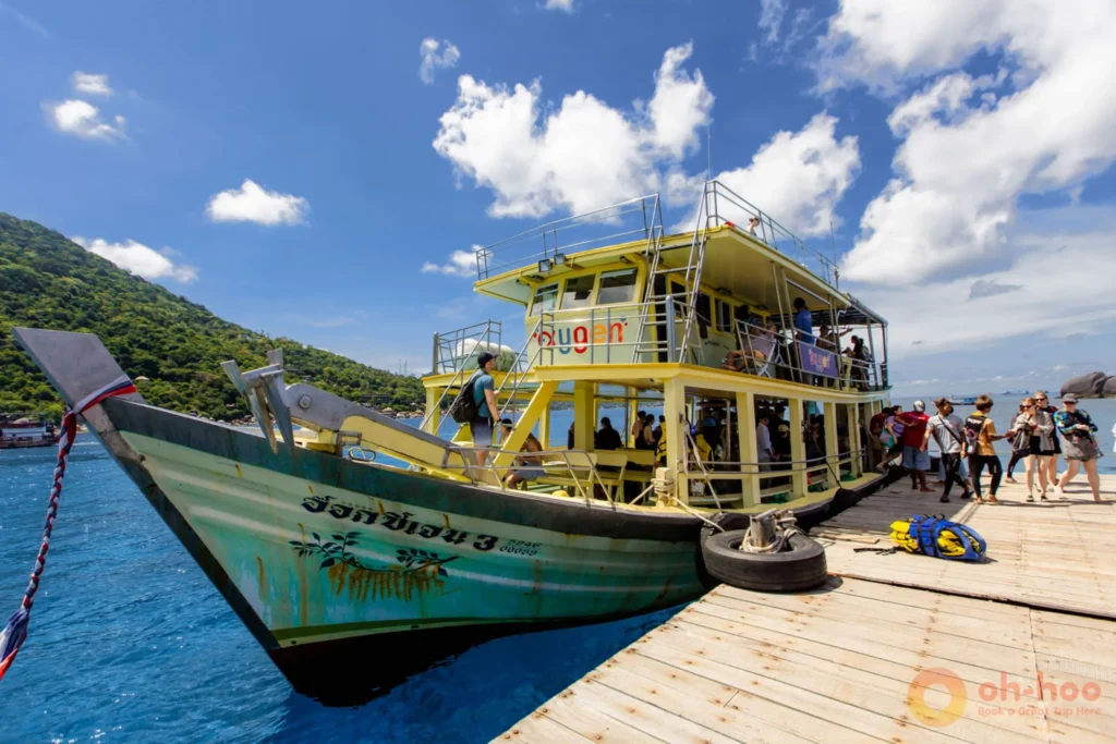 Travellers boarding a double-deck snorkeling day-trip boat at a Koh Tao pier under a bright blue sky