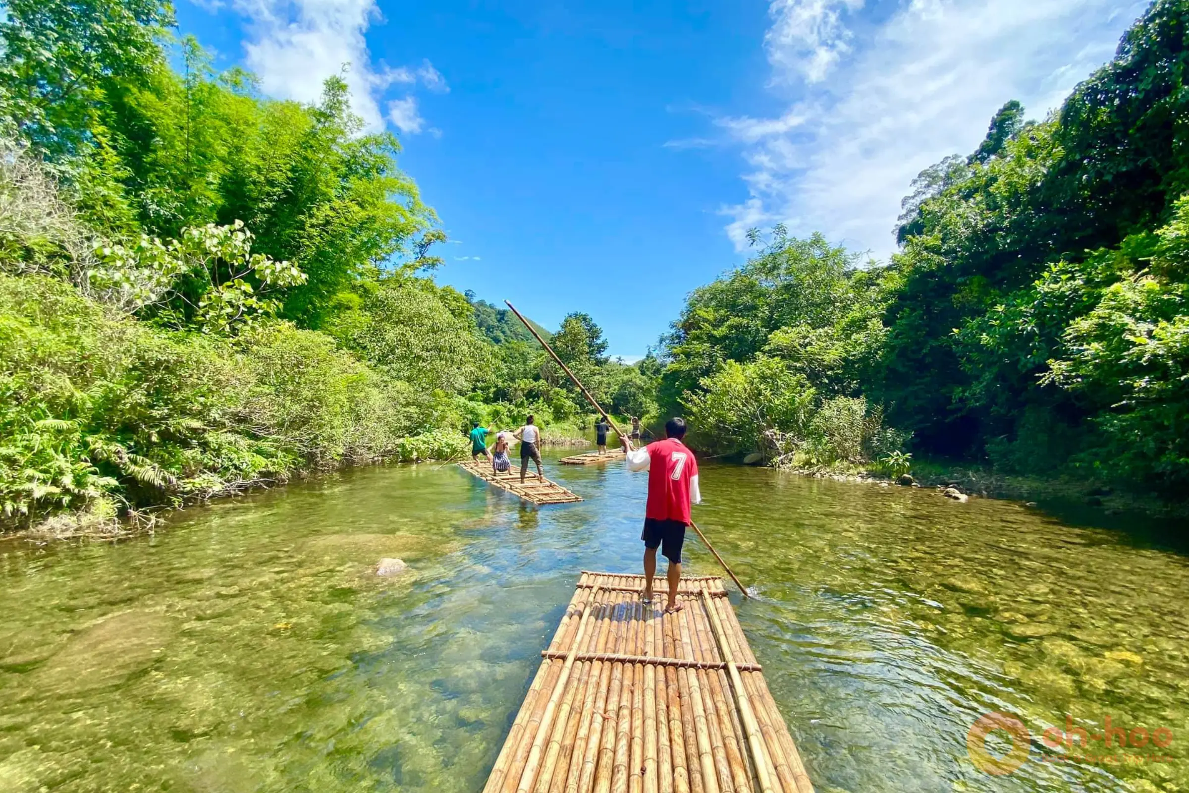 A boatman poling a traditional bamboo raft down a calm, clear jungle river on a Khao Lak bamboo rafting trip