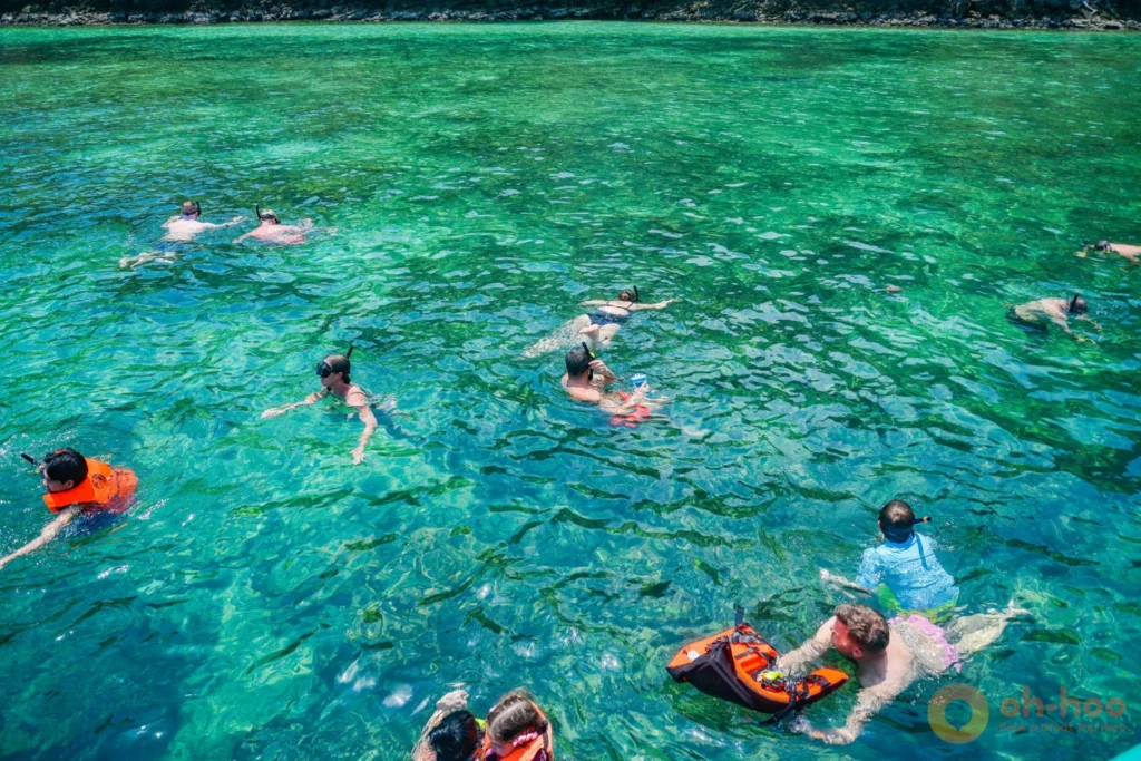 Tourists snorkeling in clear emerald ocean water near a boat on a Krabi 4 Islands tour.