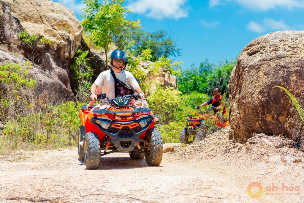 Tourist riding an orange ATV quad bike through a rocky jungle path in Koh Phangan.
