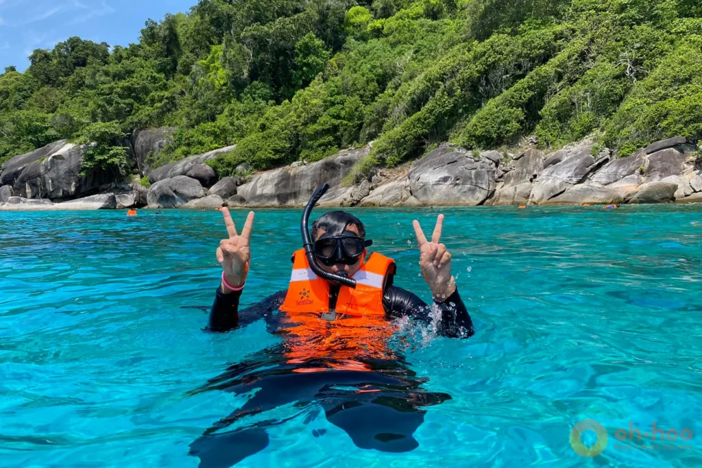 A traveler floating peacefully in the crystal-clear turquoise ocean along the lush green tropical coastline of the Surin Islands.