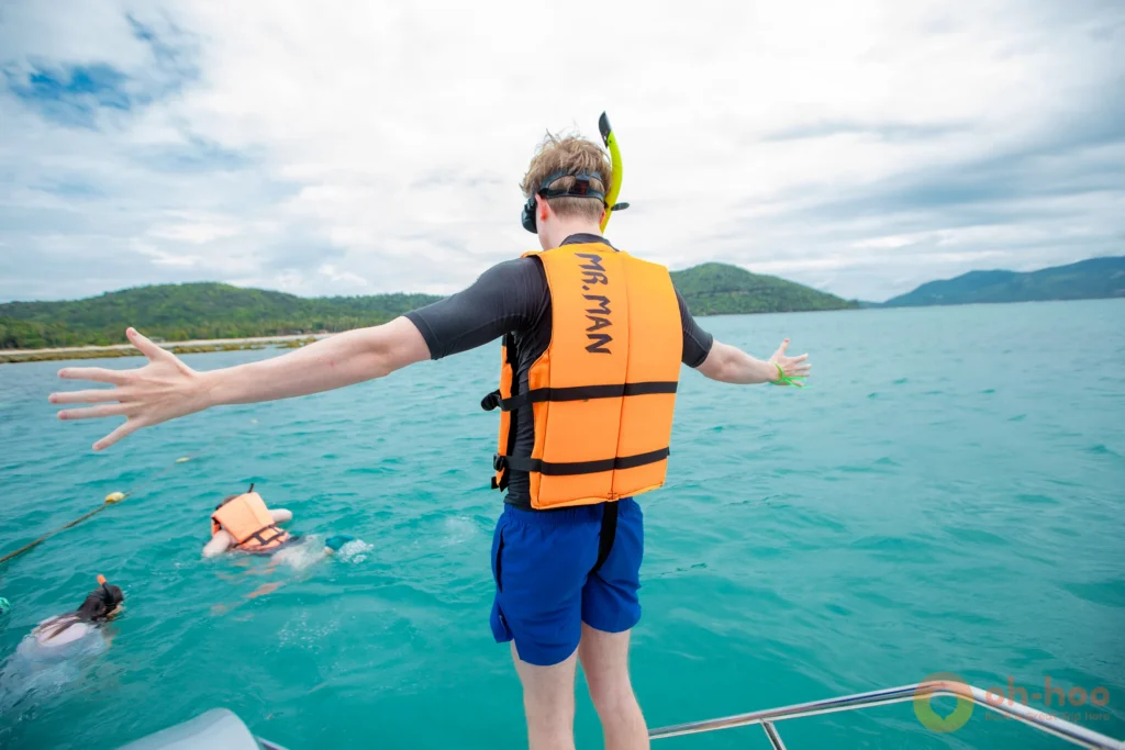 A traveler in a life jacket preparing to dive from a boat into turquoise seawater.