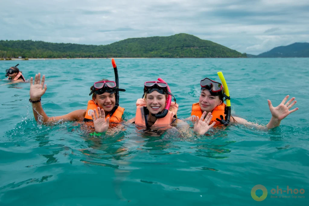 Three happy tourists snorkeling and waving in the sea while wearing life jackets.