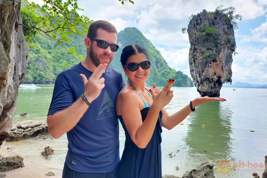 A playful couple posing with finger-gun gestures in front of the famous Koh Tapu limestone pillar at James Bond Island.