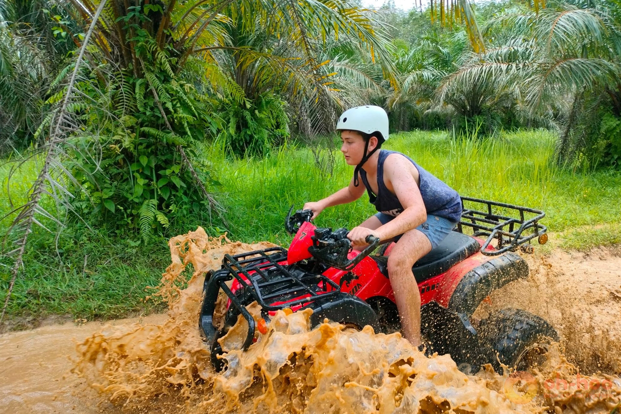 Rider on an ATV splashing through a muddy jungle trail in Khao Lak