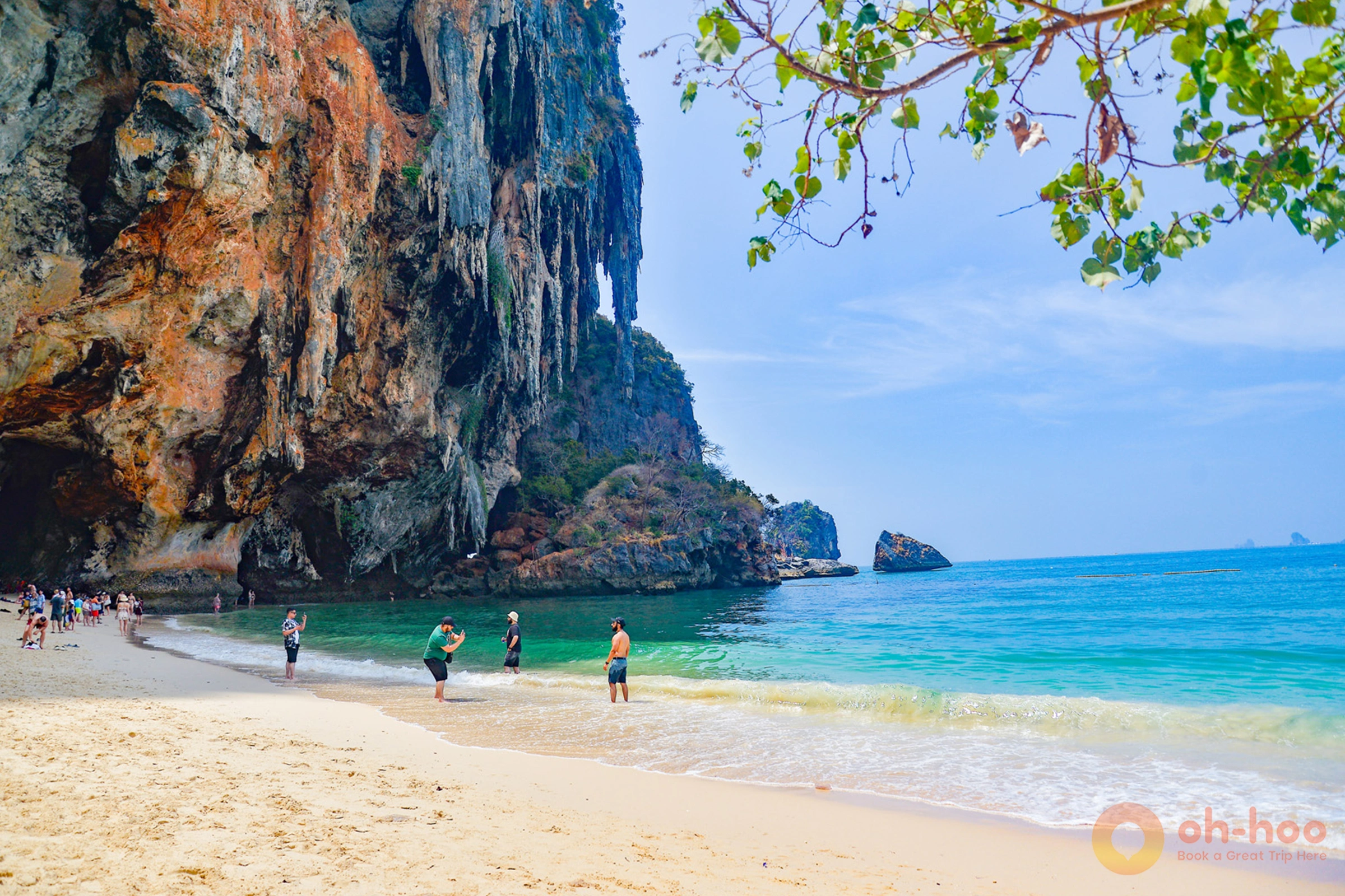 Scenic beach view in Krabi with clear blue water, longtail boats, and towering limestone cliffs under a sunny sky