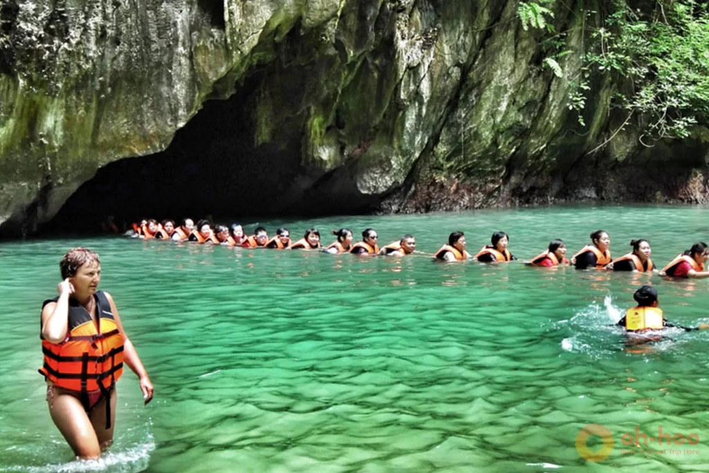 Swimmers with life jackets at the low waterline entrance to Morakot Emerald Cave