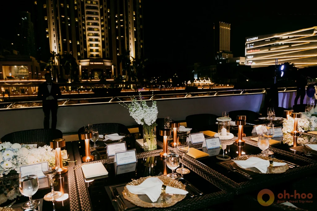 Diners at a candlelit table on the open upper deck of a Bangkok dinner cruise