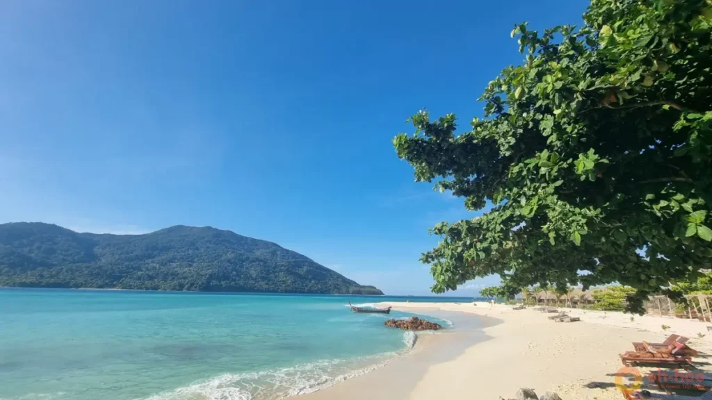 Koh Lipe Sunrise Beach with soft white sand, clear turquoise water, a longtail boat and lush tropical scenery