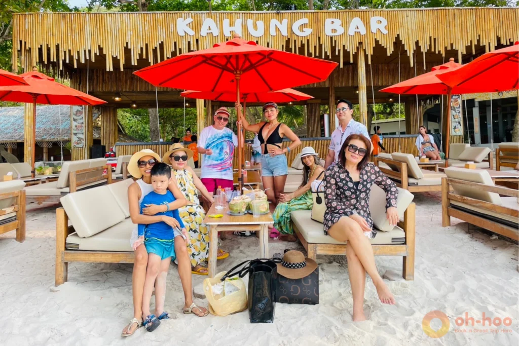 Beach loungers, umbrellas, and a busy shoreline at Coral Island Phuket during the middle of the day