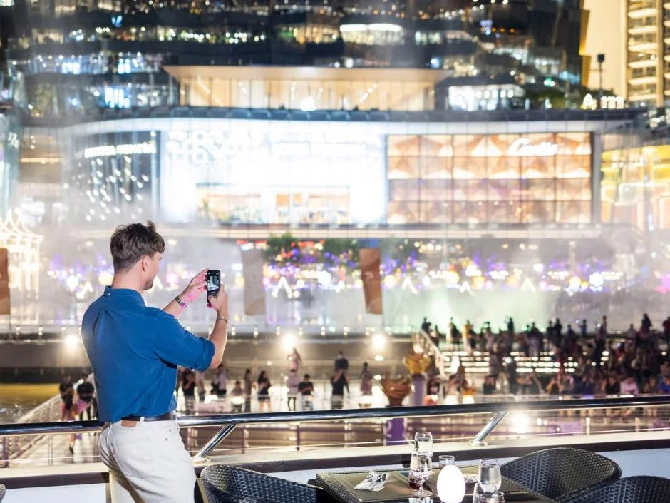 Guests watching the illuminated riverbank from the open upper deck of a Bangkok dinner cruise