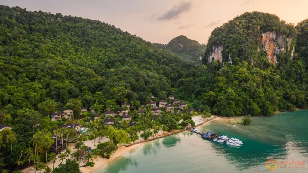 Beachfront resort beneath forested limestone cliffs on Koh Yao Noi with calm turquoise water and karst views.