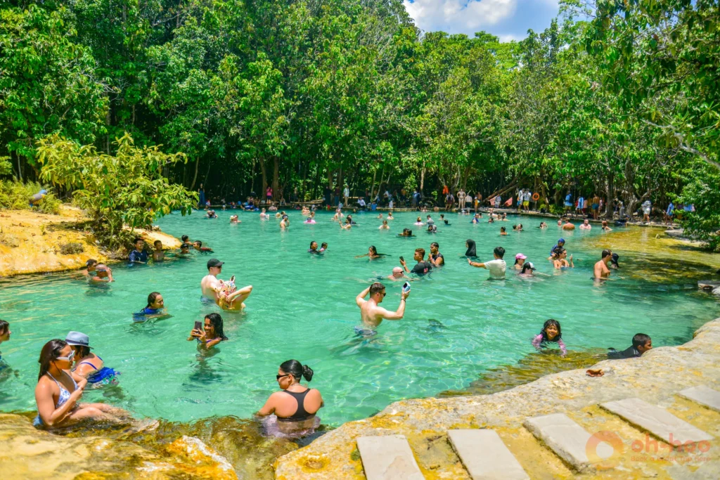Visitors swimming in the shallow green water of Emerald Pool in Krabi