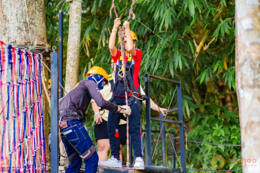 Instructor checking a young rider's harness and carabiners on a jungle zipline platform