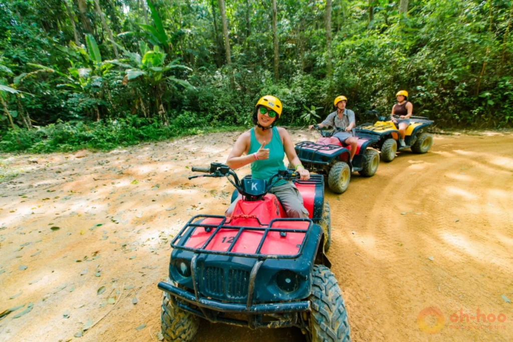 Group of riders in helmets on ATV quad bikes along a jungle dirt track in Phuket