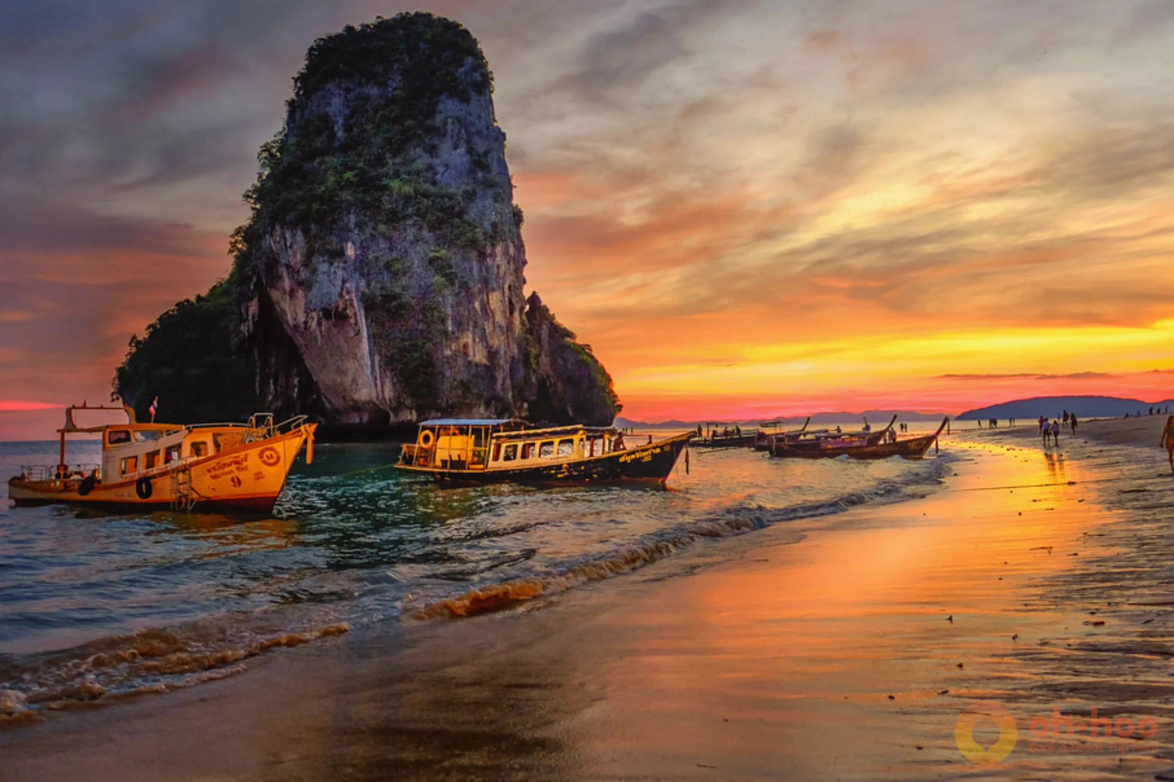 Sunset over the sea from a Krabi island beach with longtail boats on the shore and limestone karsts on the horizon