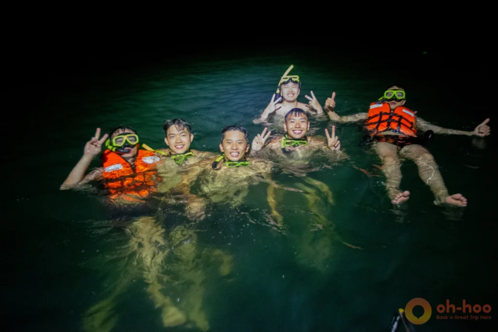 Group of swimmers in life vests and snorkel masks in the sea at night beside the boat on a Krabi plankton tour