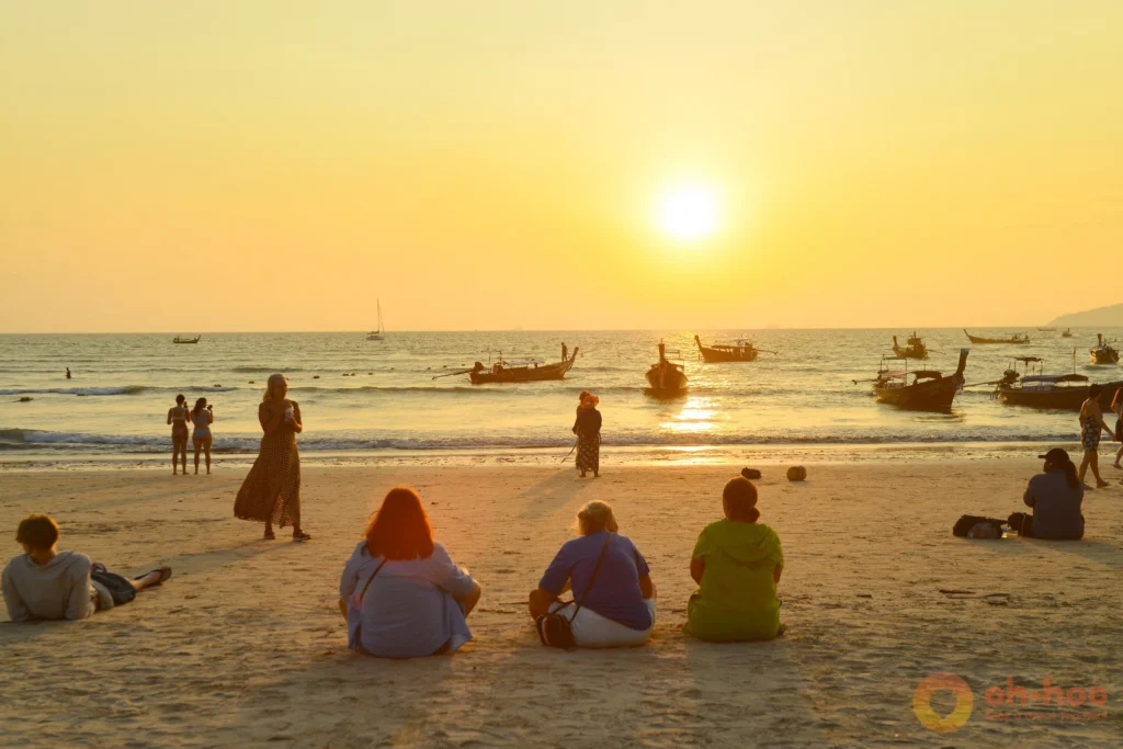 Sunset over the sea from a Krabi island beach with a longtail boat and limestone karsts on the horizon