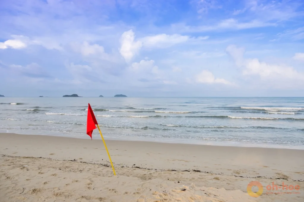 Red warning flag flying on a Phuket beach with waves breaking during monsoon season
