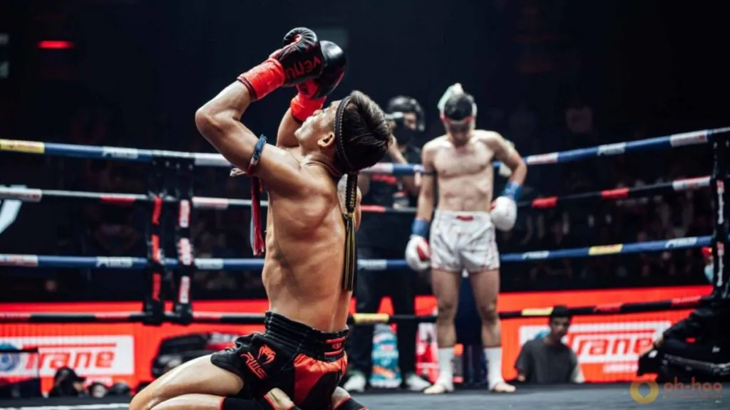 A fighter kneels on the canvas during the Wai Kru Ram Muay ritual at Rajadamnern Stadium, wearing a traditional mongkhon headband.