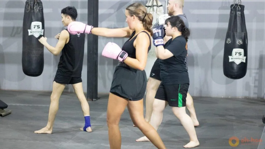 Participants practice punches together in a group training session wearing boxing gloves inside a gym.