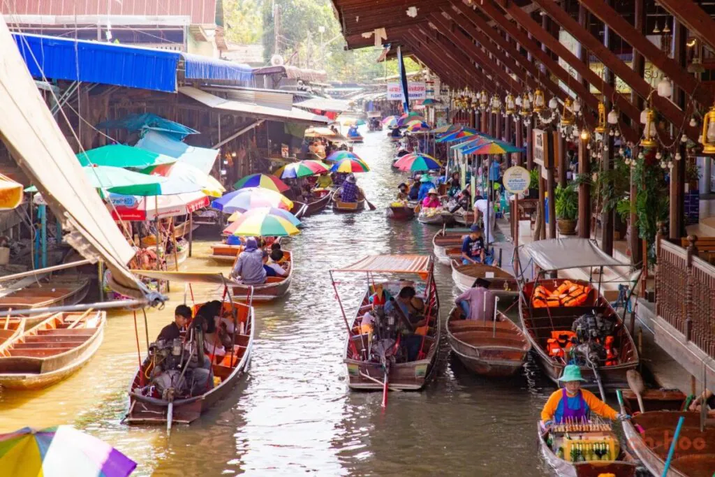 Wooden boats fill the canal at Damnoen Saduak beneath colorful umbrellas and rows of waterside shops.