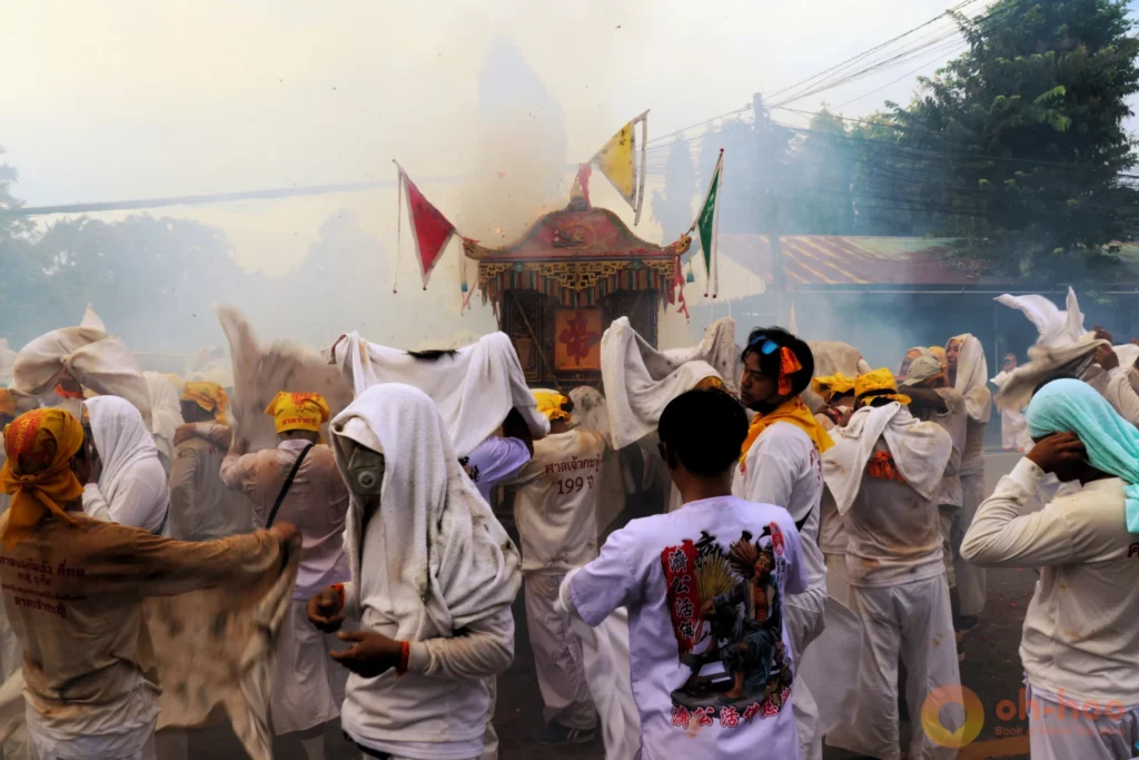 Devotees in white carrying a sedan chair through incense smoke at a Phuket shrine procession