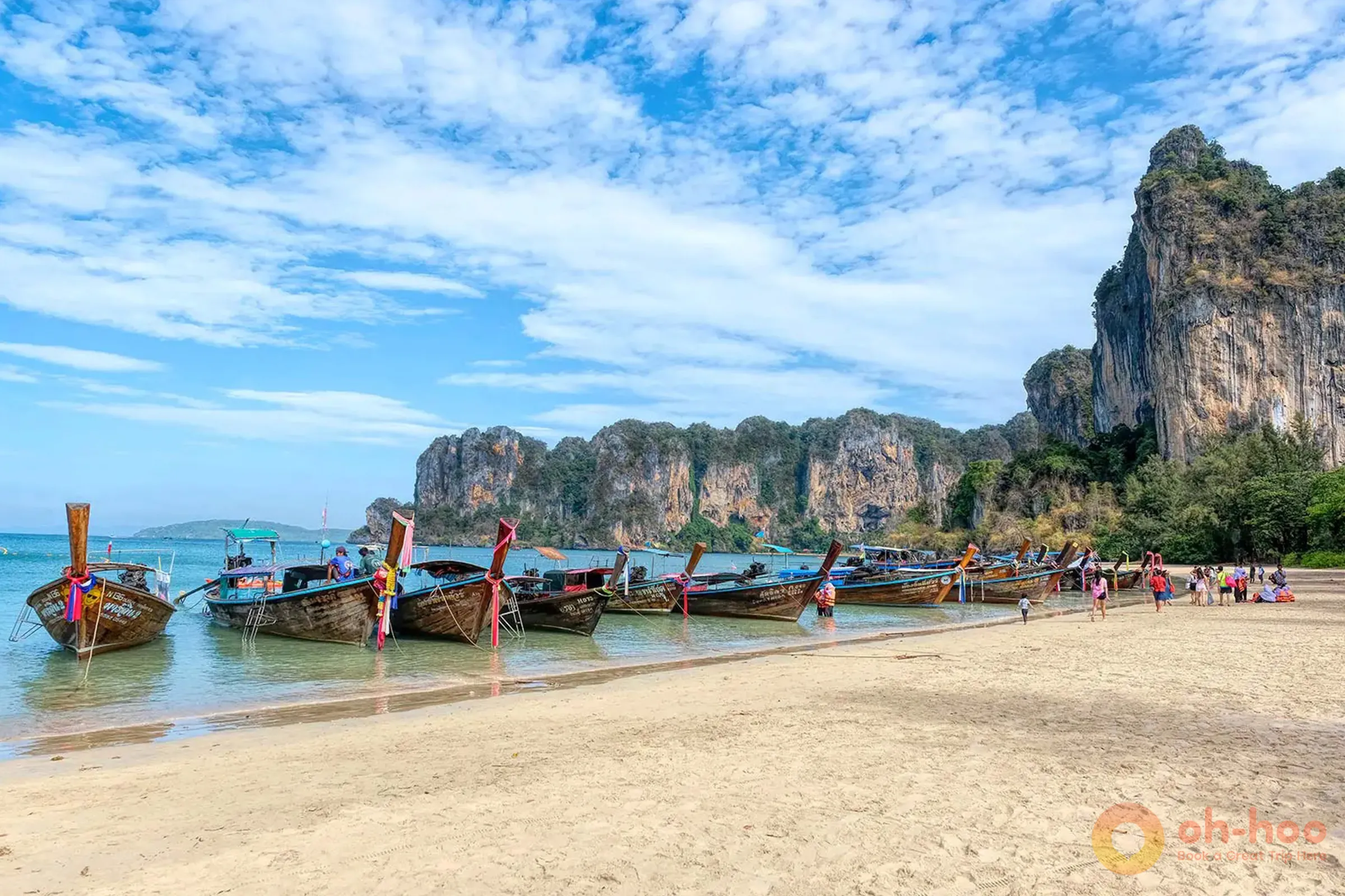 Longtail boats moored off a white sand beach with limestone cliffs near Krabi