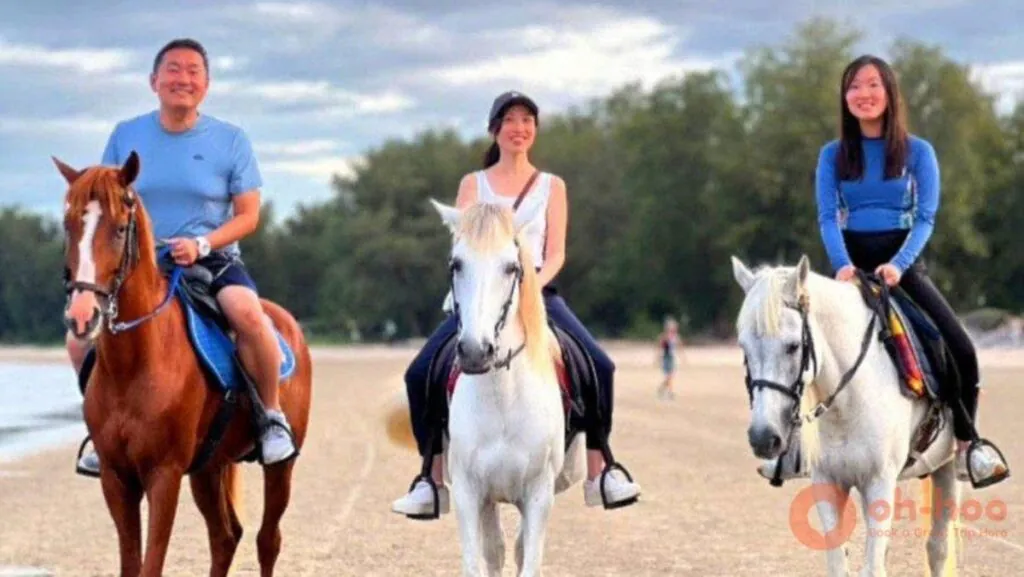 Three people smiling while riding horses along a sandy beach.