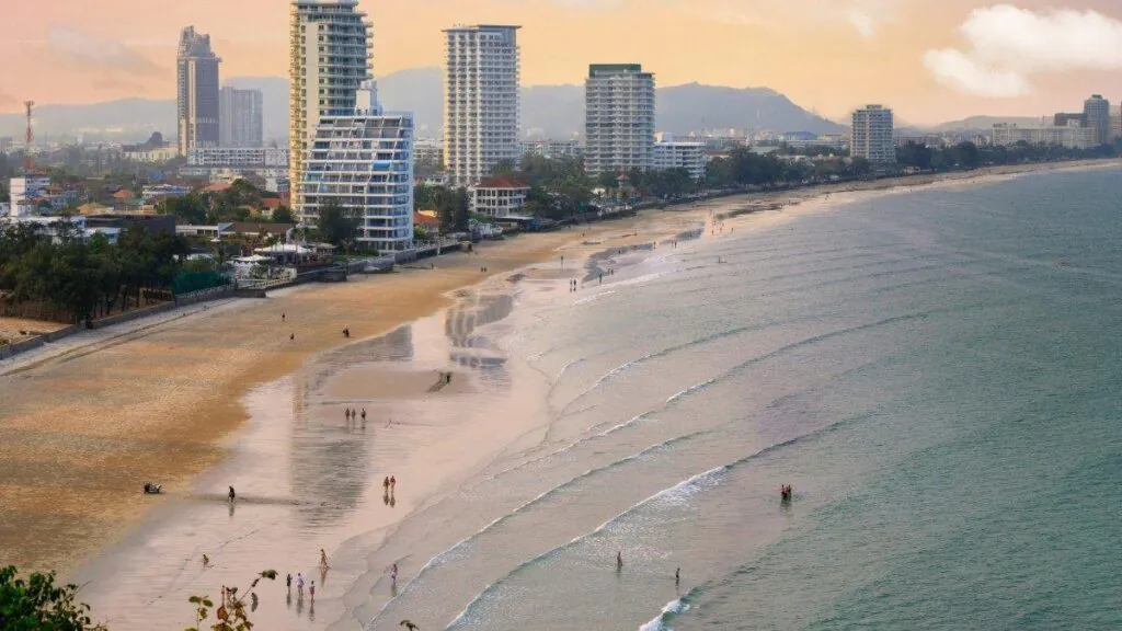 A wide sandy stretch of Hua Hin beach curves along the coastline, backed by high-rise hotels and apartments under a hazy sky.