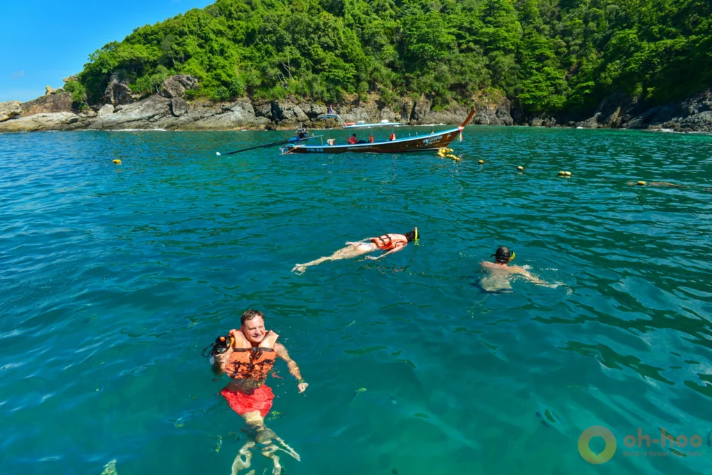 Tourists in life jackets swimming and snorkeling in shallow turquoise water at Kahung Beach, Coral Island