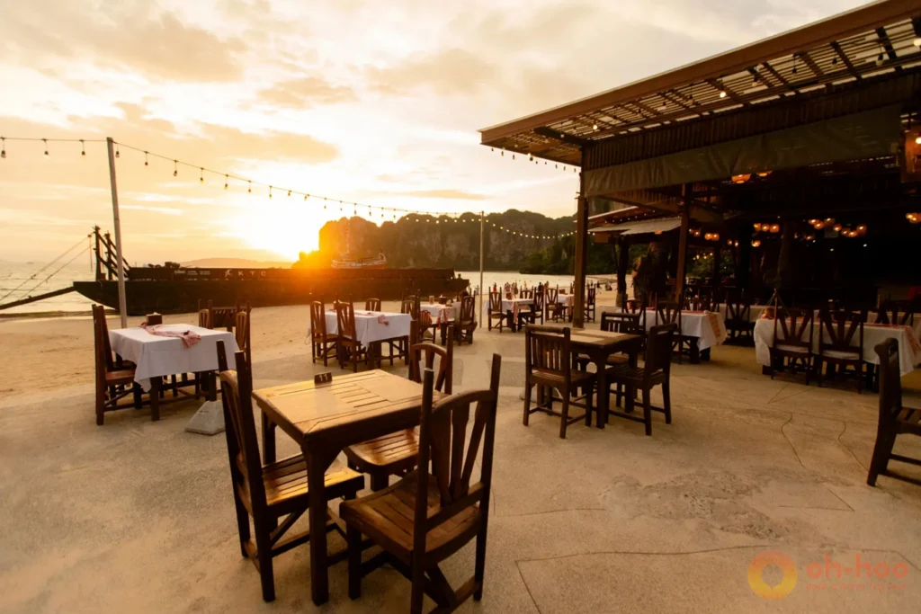 Romantic beachfront restaurant tables set up on the sand at sunset with limestone mountain views